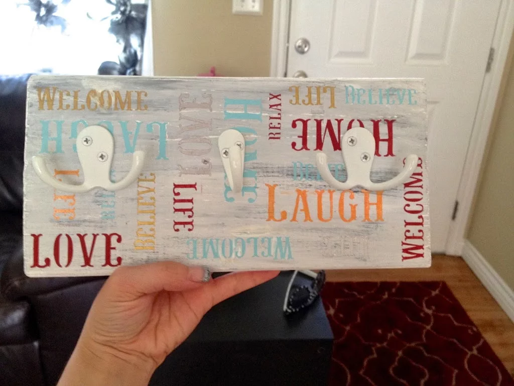 Finished DIY key holder with threshold hooks on painted rectangle wood that says welcome, laugh, life, and believe 