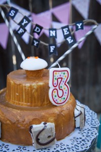 Peanut Butter cake with a small cupcake on top, a number three candle, and a banner than says Sydney Fyfe