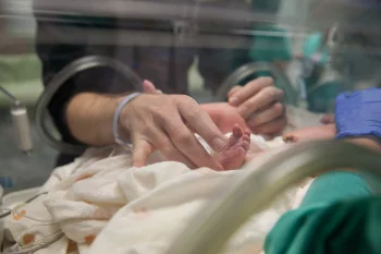 Daddy and MeDad touching babies foot in NICU container 