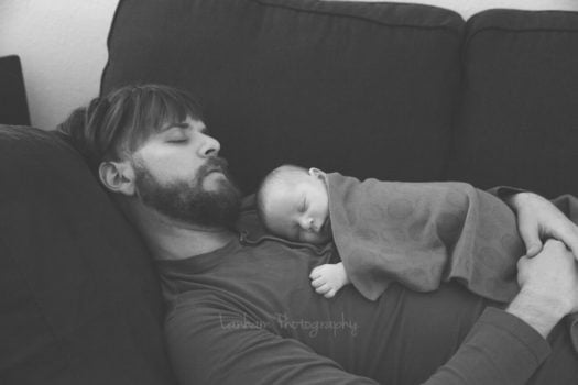 Man with baby on chest both sleeping on couch 