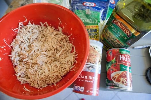 Shredded Chicken in red bowl, can of bread crumbs, can of pasta sauce, extra virgin olive oil, mozzarella cheese 