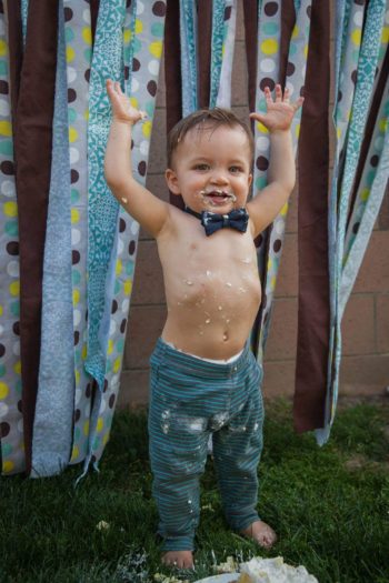 Toddler boy wearing bow tie on grass with frosting on face 