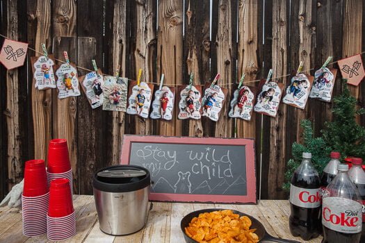 Custom pictures hanging on a banner on the fence and stay wild my child sign on table with snacks and beverages 