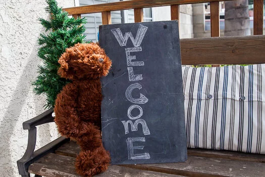 Welcome chalkboard sign held by teddy bear on bench 