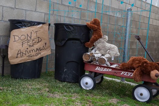Stuffed wooden animals on wagon going for trash with sign titled Don't feed the animals trash only