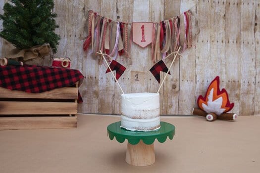 Three tier white cake with number 1 hanging on the back wall with small Christmas tree in background 