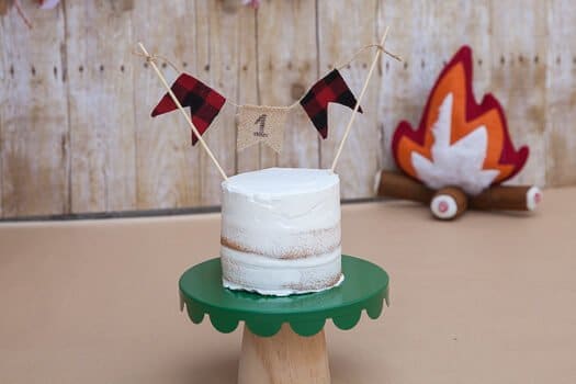 Three tier white cake with number 1 hanging on green pedestal and toy fire in background