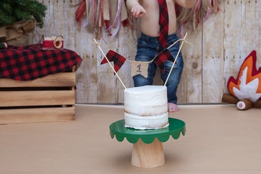 Three tier white cake with number 1 hanging and toddler with jeans in background 