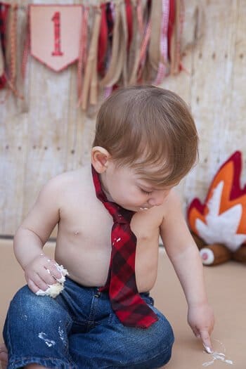 Toddler boy eating cake and wearing tie and jeans 