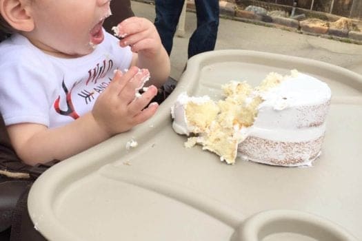 Toddler boy eating white cake in toddler chair 