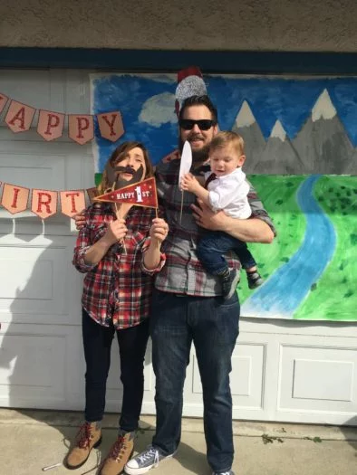 Family of three holding happy 1st birthday signs in front of decorated garage door