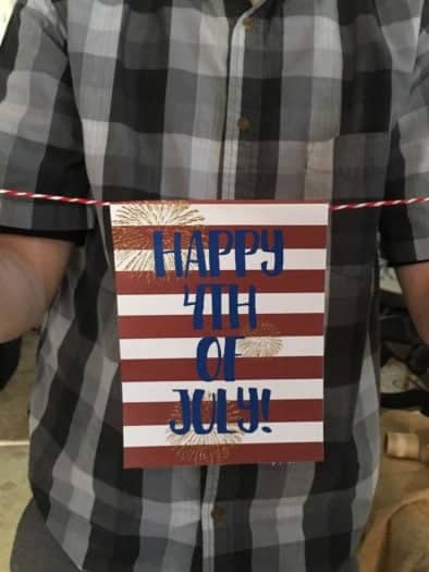 Man wearing flannel holding paper with threaded string with happy 4th of July printable 