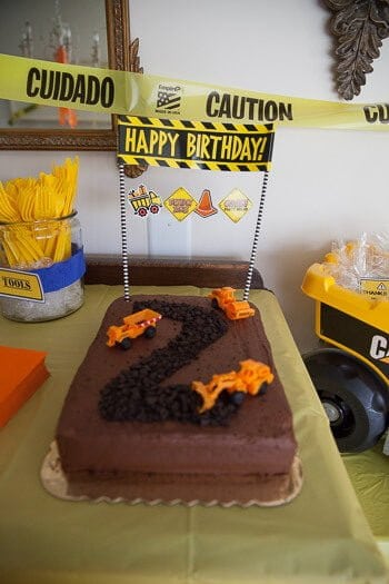 Cake with 2 made with oreo crumbs and toy construction cars on it and caution sign that says happy birthday