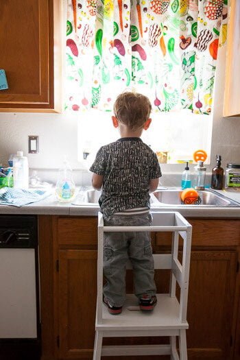Toddler standing on Ikea tower looking over sink