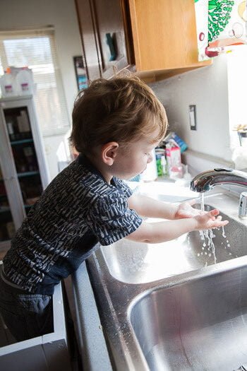 Toddler standing on Ikea tower washing hands in sink