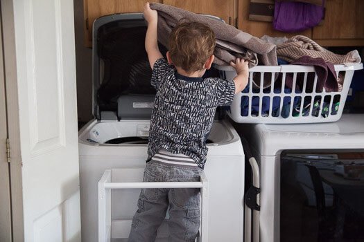 Toddler standing on Ikea tower putting laundry in washing machine