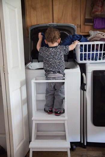 Toddler standing on Ikea tower putting laundry in washing machine