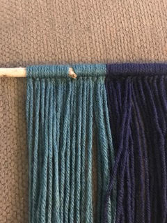 looping each blue and teal strand of yarn to the wood stick 