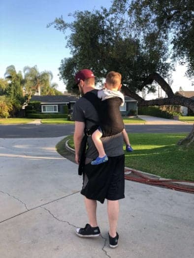 John with toddler in carrier on back walking in driveway 