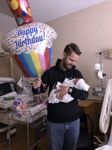 photo of dad with new baby and a birthday balloon in hospital room 