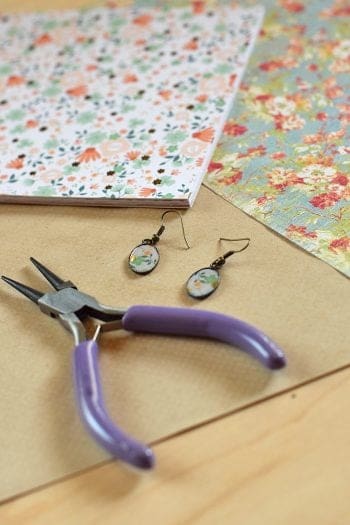 Handmade oval earrings with flower card stock paper in the oval earrings on table with card stock paper and needle-nose pliers 
