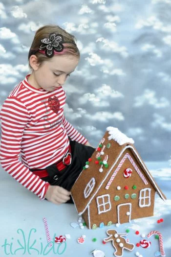 Little girl with flower headband and striped shirt playing with felt gingerbread house
