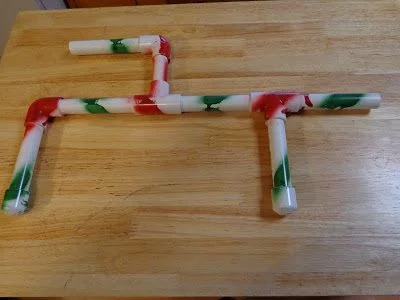 pvc pipe marshmallow shooter with red and green painted stripes laying on wood table 