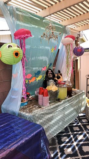 Mermaid and pirate party decorations including hanging jellyfish and drinks in jars and ups on table