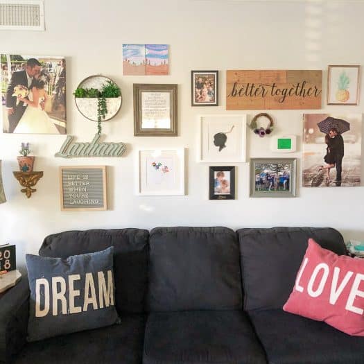 Wall filled with 18 items of pictures and letter frames over a couch with a pillow labeled dream and a pillow labeled love