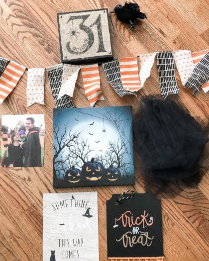 Halloween gallery items including a 31  with a spider wall hanging. A hanging of dark pumpkins with moon background. A piece of black fabric. A banner. A picture of a couple. A printable found in the VIP library.
