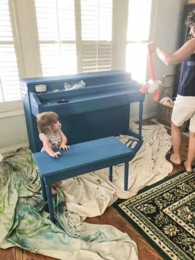 Finished blue painting of piano with toddler next to it 