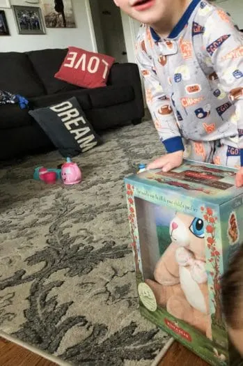 Toddler wearing pajamas standing with binka bear in package in living room 