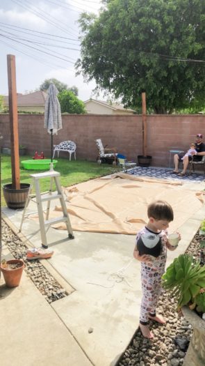 Backyard being set up for the shade cloths with toddler drinking milk 