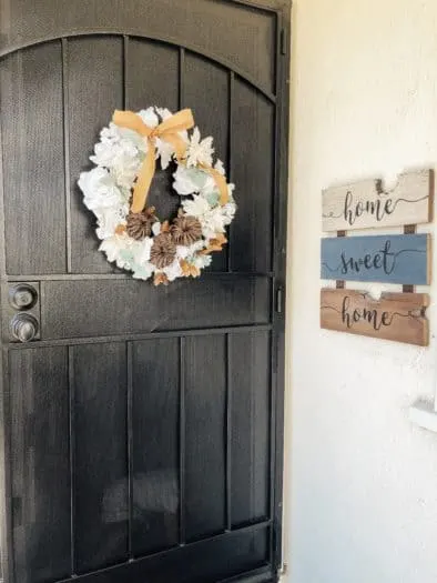 Finished seasonal wreath hanging on black door. home sweet home sign hanging on wall next to it