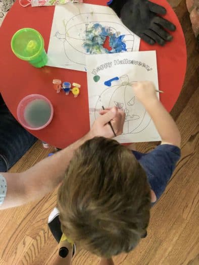 toddler painting a pumpkin coloring sheet that says happy halloween