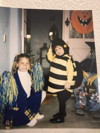 Two young girls dressed in Halloween costumes. One is a cheerleader and the other a bee.