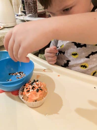 toddler putting sprinkles on a cupcake
