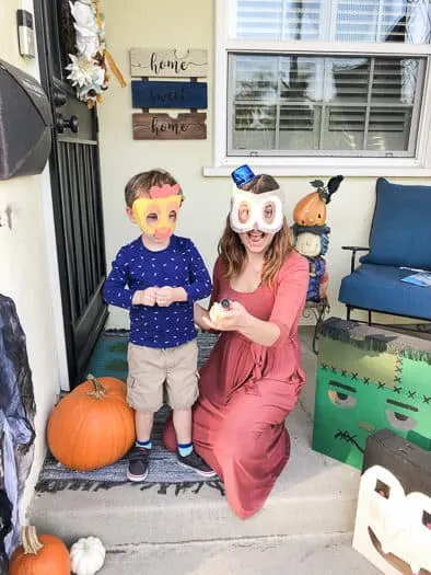 Woman in a dress wearing a owl mask aiming a confetti popper at camera with a party hat on standing next to a little dressed nicely wearing a chicken mask