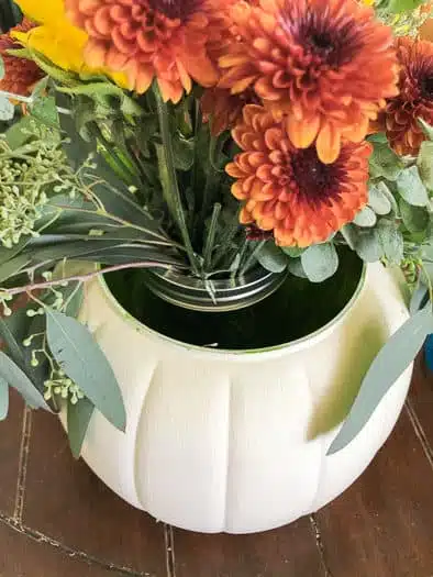 aerial view of a white pumpkin with a mason jar in the center holding red flowers