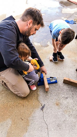 father and kids working on a piece of wood together 