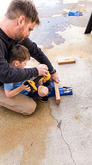 father and son using a power drill on a wood block together