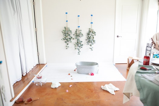 Behind the scenes image showing eucalyptus leaves hanging on a wall with a galvanized tup in the center on white paper