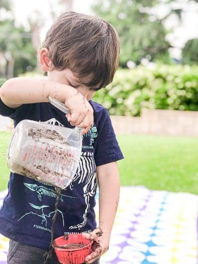 Kid pouring mud out of a measuring cup into a small round ramekin.