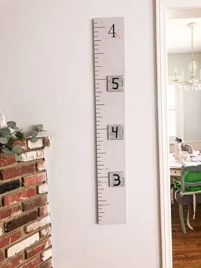 A growth chart that is grey in color hanging on a wall next to the edge of a brick fireplace