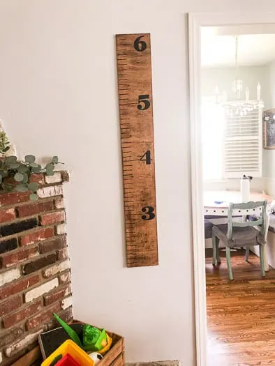 Completed growth chart with the numbers 3 to 6 hanging on the wall next to the edge of a brick fireplace. Can see a kitchen table in the background.