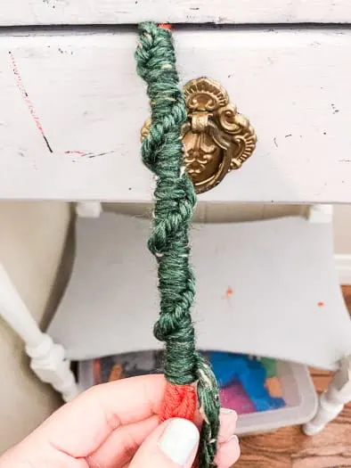 Green yarn wrapped in a half square knot twist around an orange braided yarn.
