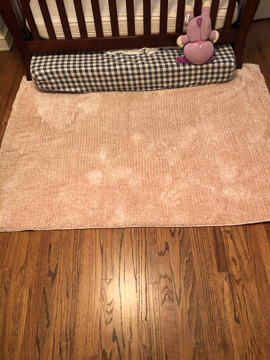 Pink rug clean on a wood floor with a crib sitting on it.