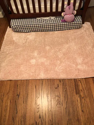 Pink rug clean on a wood floor with a crib sitting on it.