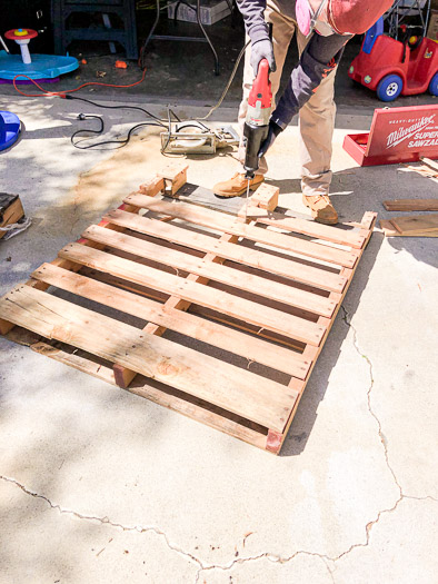 Man using a saw to to cut a pallet board apart.