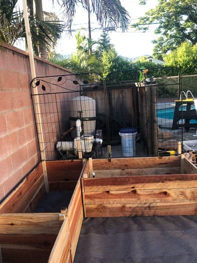 empty redwood garden boxes with fencing attached to the boxes and pool equipment in the background